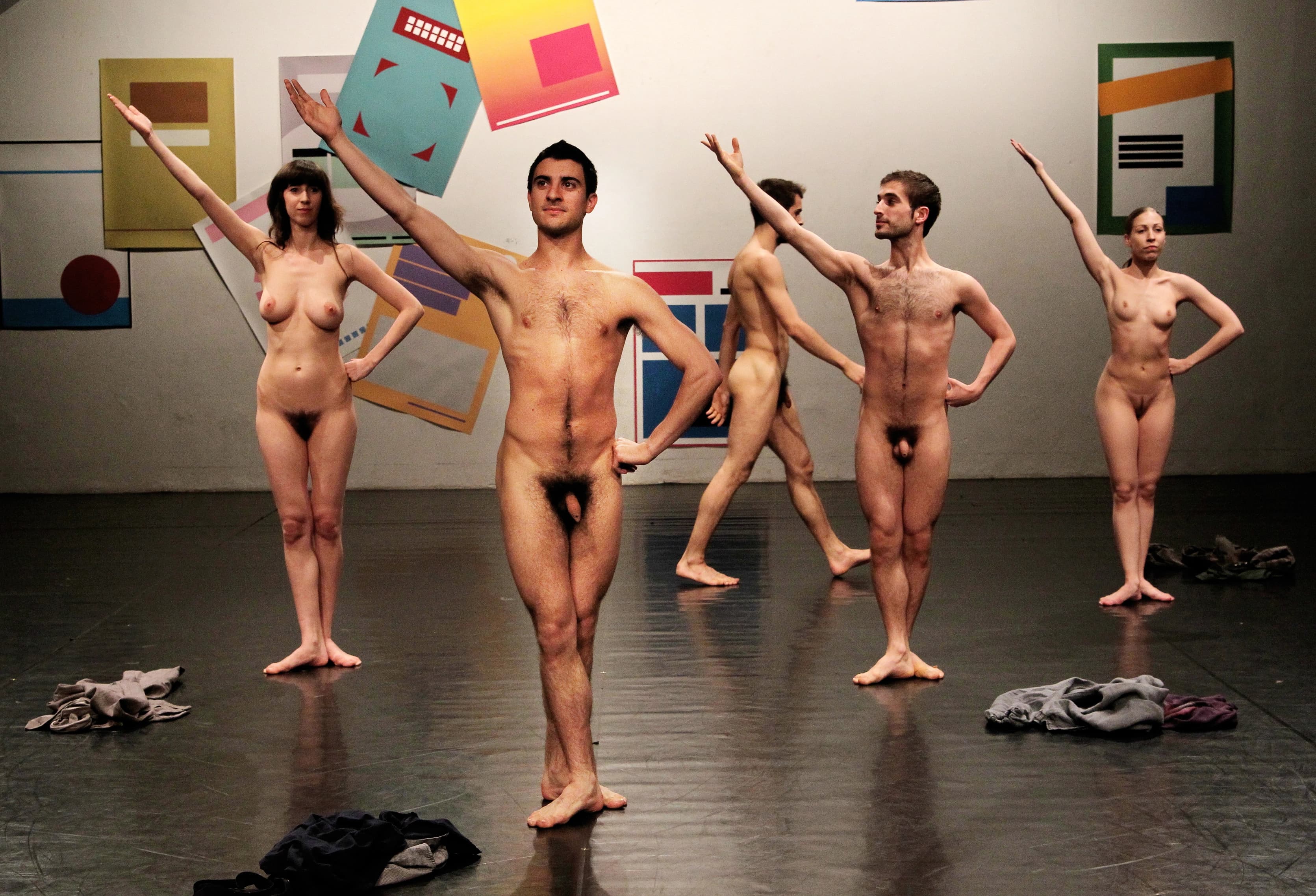 Five people on stage all naked, four facing the audience and holding the same position, the fifth one walking in the background