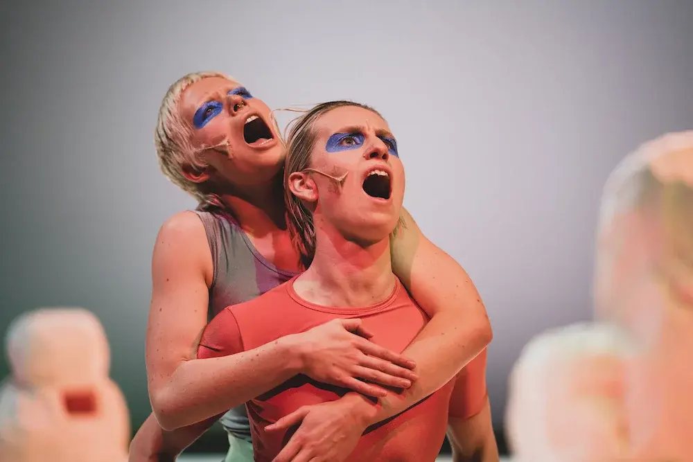 Tasha climbing on Hanna's back as they sing with their mouths wide open