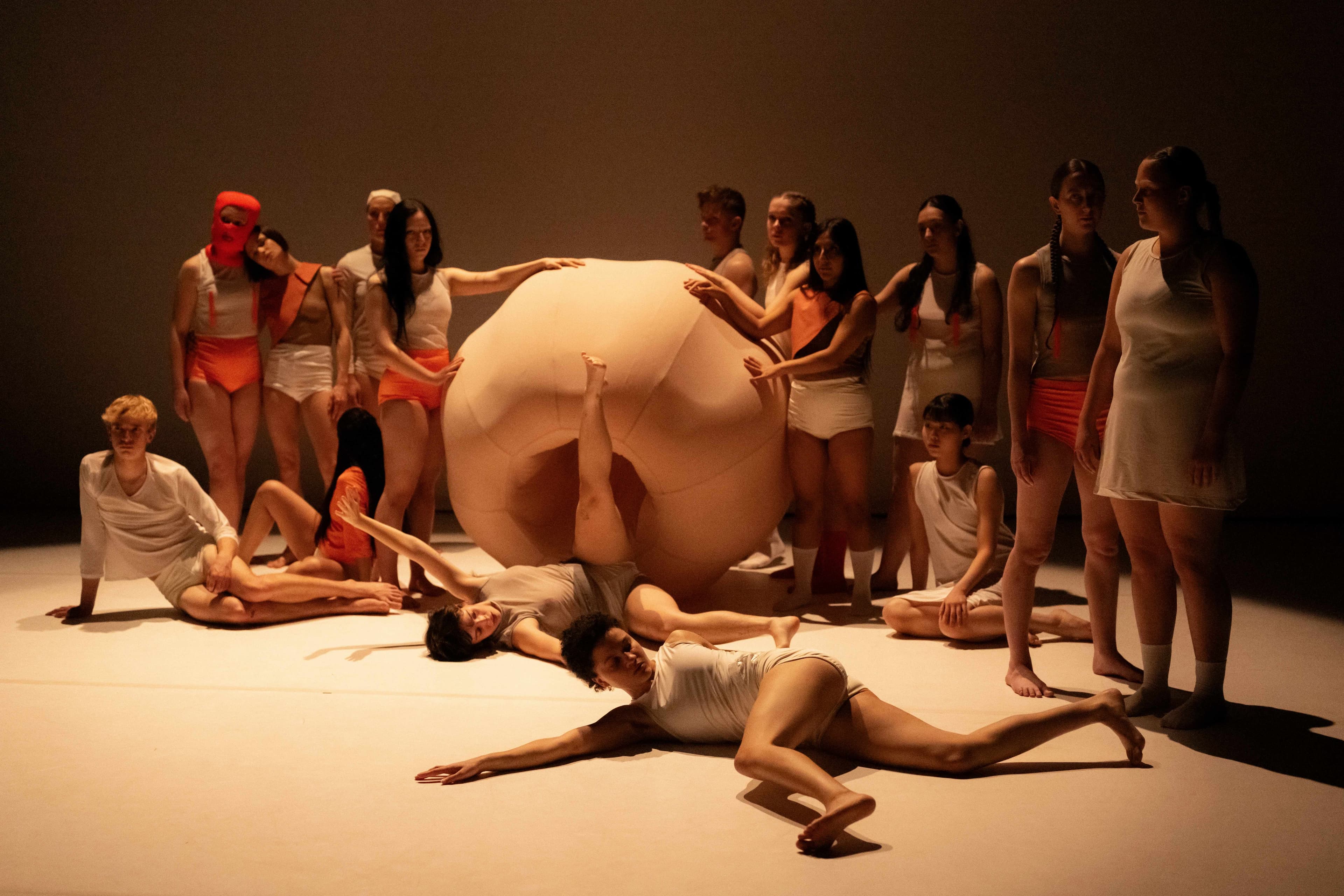 Whole cast in costumes posing as a surreal tableaux with props and warm lighting