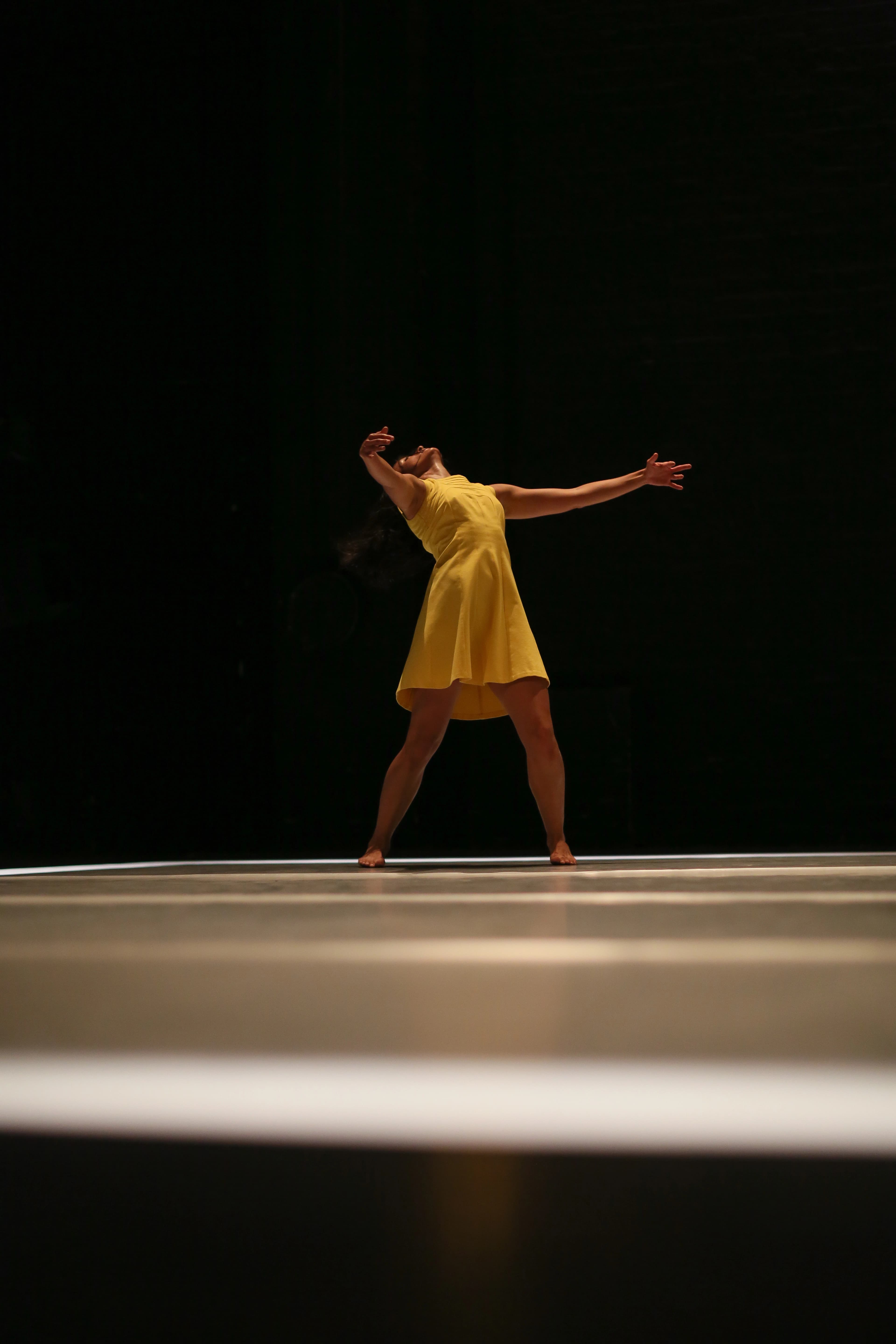 A woman in a yellow dress standing in the middle of the stage with her arms open to the side and the head tilted back